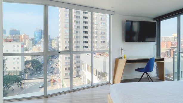 Ein modernes Hotelzimmer mit großem Fenster, einem Bett, einem Schreibtisch und einem Sessel.