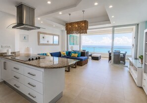 Una cocina moderna con una isla central, un comedor con vistas y una sala de estar con sofá y cojines.