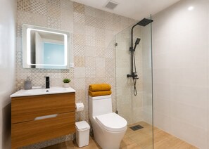 A modern bathroom with a glass shower enclosure, a wooden vanity, and a white toilet. - Best View 8th Floor| Beachfront| Fast Wifi| Pool (Juan Dolio)