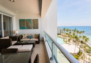 A balcony with wicker furniture, a view of the beach, and tropical-themed wall art.