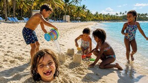 A beach scene with children playing in the sand, palm trees, and clear blue water.