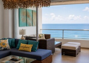 A living room with a sofa, cushions, a glass coffee table, wicker furniture, a lamp, and a view of the ocean. - Best View 8th Floor| Beachfront| Fast Wifi| Pool (Juan Dolio)