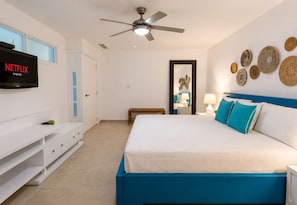A bedroom with a bed, a TV, a ceiling fan, a bedside table with a lamp, and decorative wall art.