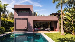Una casa moderna amb piscina, mobiliari d'exterior i vegetació exuberanta.