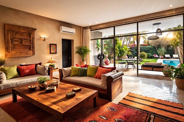 A modern living room with a sofa, coffee table, and a view of a pool and garden.
