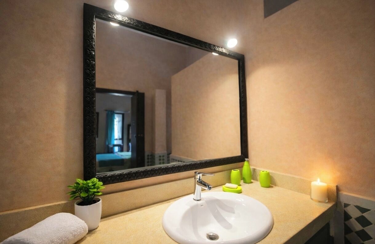 Ein Badezimmer mit einem großen Spiegel, einem weißen Waschbecken, einer kleinen Topfpflanze und Toilettenartikeln auf der Ablagefläche.