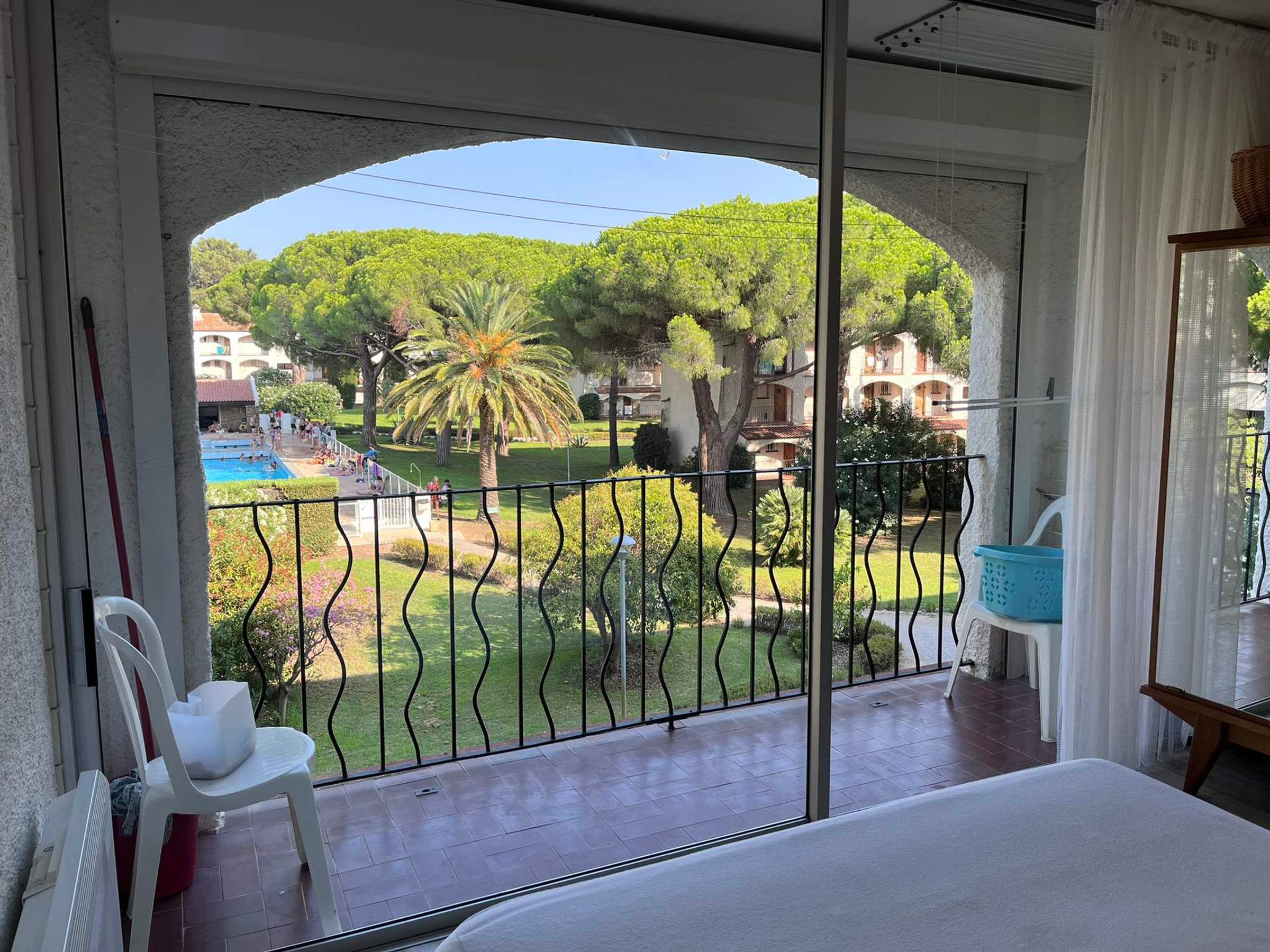 Un balcón con vistas a una piscina, vegetación y un edificio al fondo.