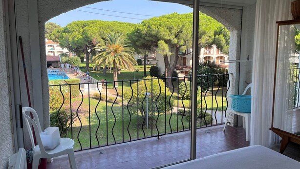 Ein Balkon mit Blick auf ein Schwimmbecken, viel Grün und ein Gebäude im Hintergrund.