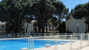 Ein Swimmingpool mit weißem Zaun, umgeben von Bäumen und einem Gebäude mit Ziegeldach.
