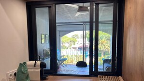 Ein Zimmer mit einem Holztisch, einem kleinen, fischförmigen Gegenstand, einem weißen Gerät und einem Fenster mit Blick auf einen Pool und Grünflächen.