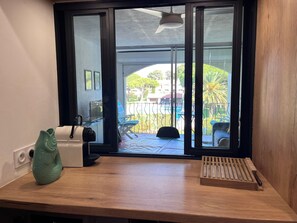 A room with a wooden desk, a small fish-shaped object, a white device, and a window with a view of a pool and greenery. - Apartment for 6, near sea with balcony and garden (Argelès-sur-Mer)