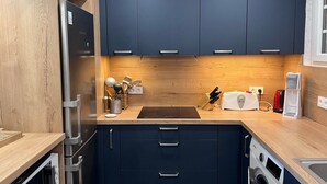 Eine kleine Küche mit dunkelblauen Schränken, einer Holz Arbeitsplatte, einem eingebauten Backofen, einer Waschmaschine und einem Toaster.