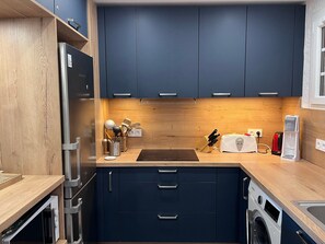 A compact kitchen with dark blue cabinets, a wooden countertop, a built-in oven, a washing machine, and a toaster. - Apartment for 6, near sea with balcony and garden (Argelès-sur-Mer)