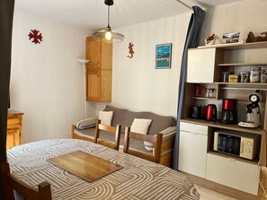 A compact living space with a bed, a dining table, a kitchenette, and a hanging light fixture.