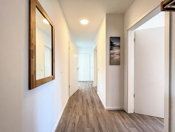 Ein Korridor mit Holzboden, weißen Wänden und einem gerahmten Bild an der Wand.