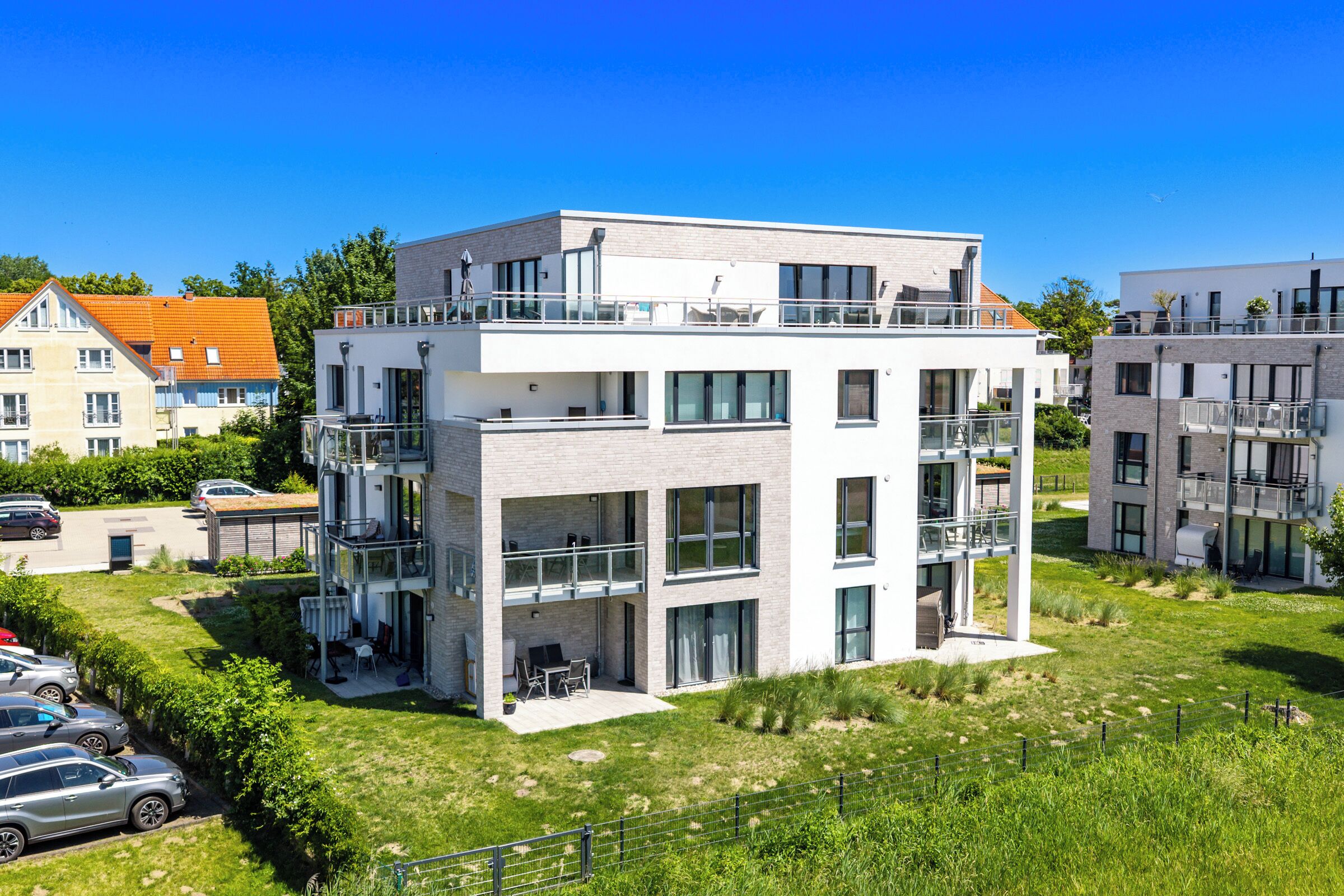 A modern multi-story residential building with balconies, a parking area, and a well-maintained lawn.