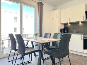 Une cuisine moderne avec des meubles blancs, une machine à café noire et un coin repas comprenant une table en bois et des chaises noires.