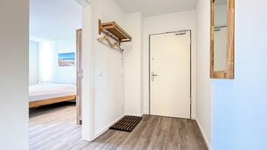 Un pasillo con suelo de madera, una puerta blanca y un estante pequeño de madera.