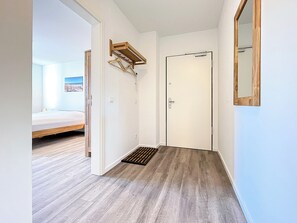 Ein Flur mit Holzboden, einer weißen Tür und einem kleinen Holzregal.