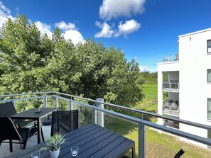 Uma varanda com mesa e cadeiras, com vista para uma área gramada e um edifício branco.