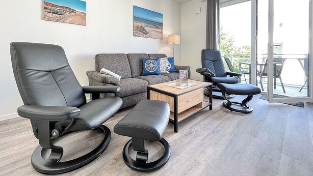 Habitación de hotel moderna con sofá, dos sillones negros, una mesita de centro y un balcón con vistas.