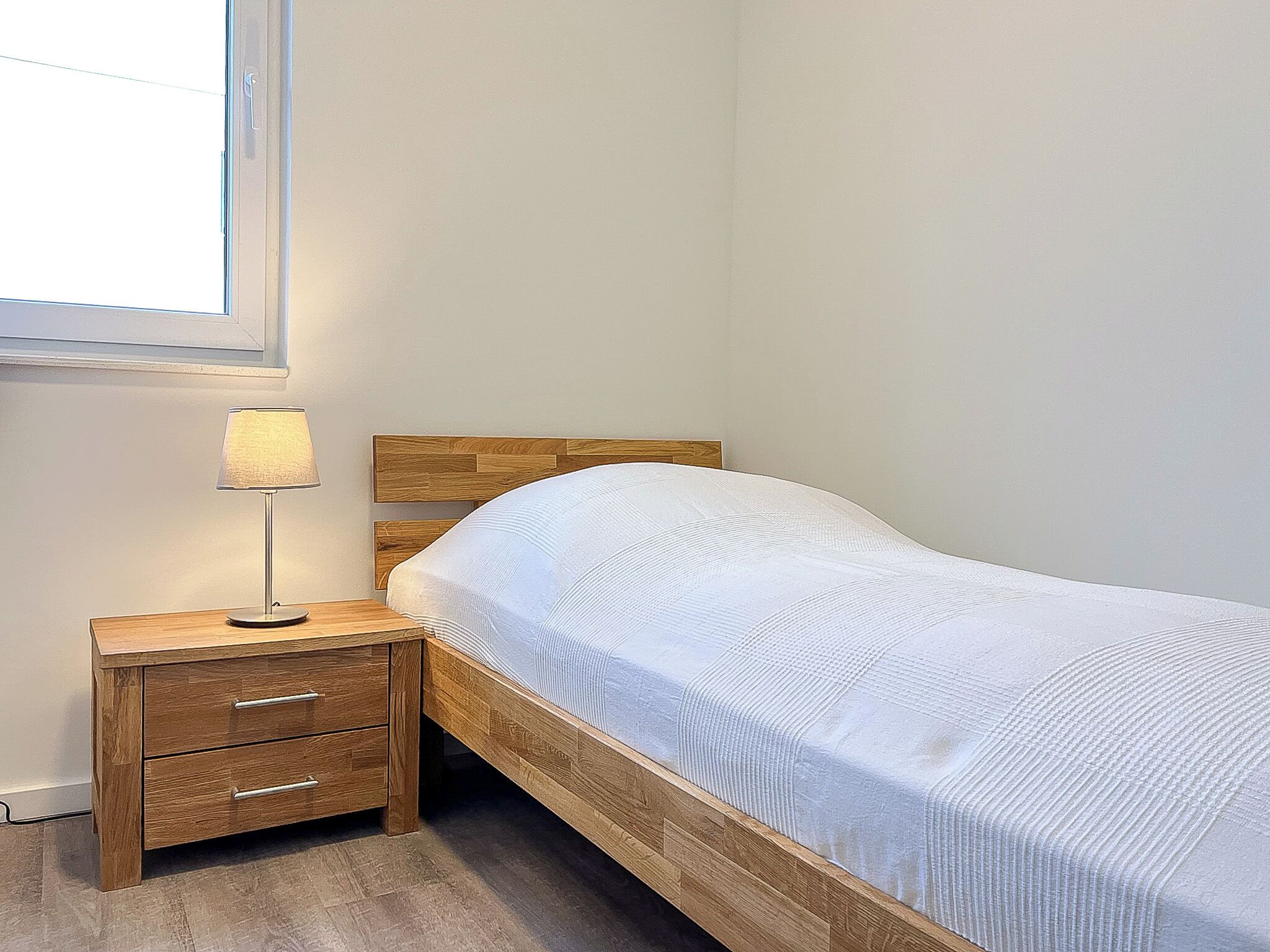 A single bed with a wooden headboard, a bedside table with drawers, and a lamp.