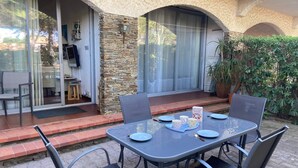 Een terras met een tafel en stoelen, een stenen muur en een glazen deur die naar een kamer leidt.