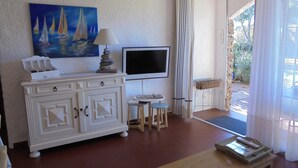 Een kamer met een witte kast, een schilderij van zeilboten, een televisie, een klein tafeltje en een bank.