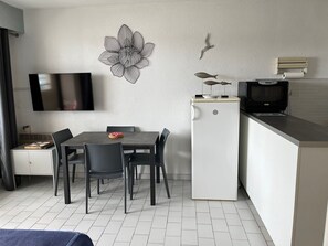 Kompakti oleskelutila, jossa on ruokapöytä, tuolit, taulutelevisio, jääkaappi ja mikroaaltouuni.