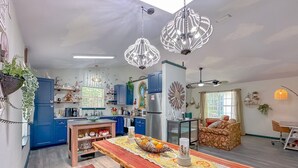 A modern kitchen with blue cabinets, a wooden dining table with a lace tablecloth, and decorative hanging lights. - Game Room-Dogs-Fence yrd- King Bed (Tallahassee)