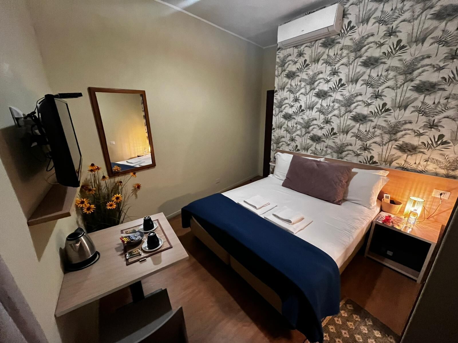 A hotel room with a bed, bedside table, desk, chair, and a wall-mounted TV.