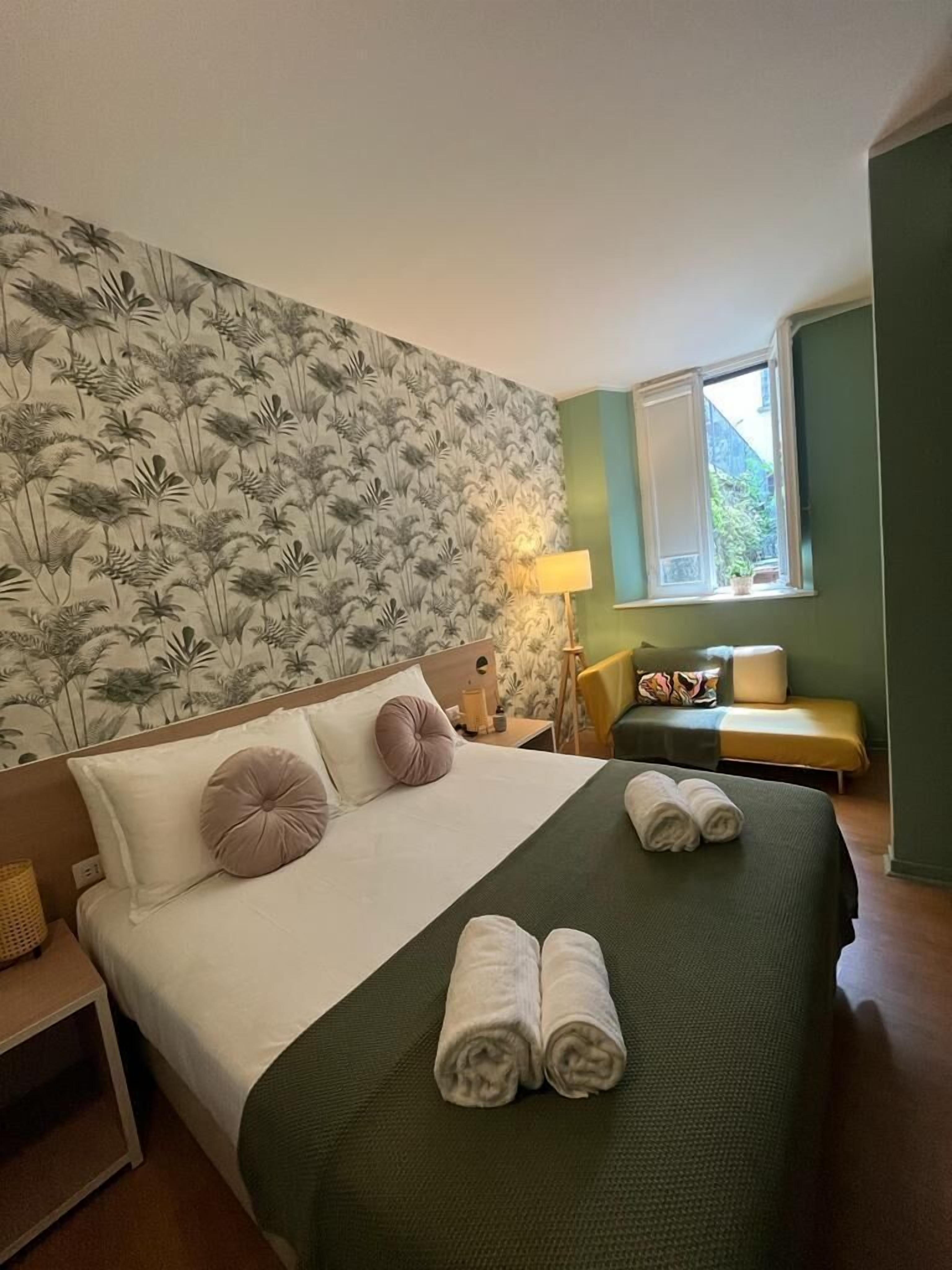 Een hotelkamer met een groot bed, een nachtkastje, een lamp, een raam met uitzicht en een groene wand.