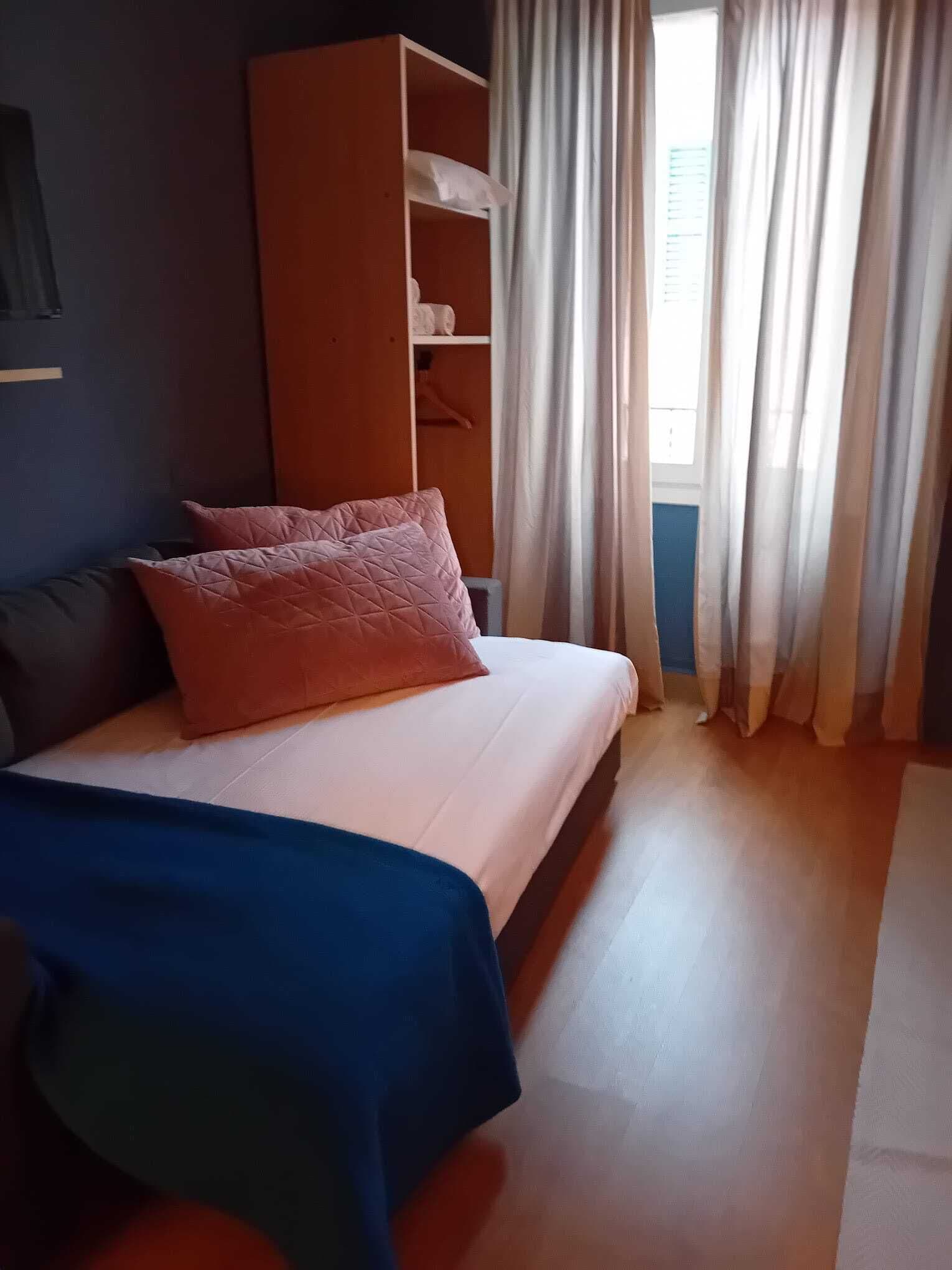 A bedroom with a bed, a wardrobe, and a window with curtains.