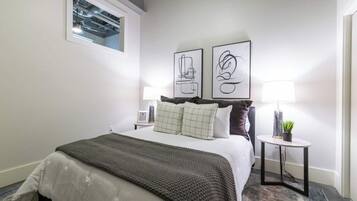 A hotel room with a bed, a nightstand, a lamp, and two framed artworks on the wall.