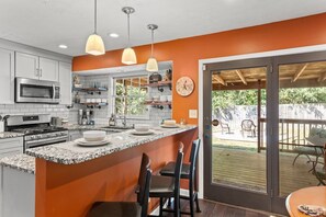 Una cocina con armarios blancos, encimera de granito e iluminación colgante. Hay una zona de comedor con una mesa y sillas.
