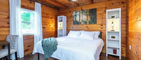 A wooden cabin bedroom with a bed, a chair, and a desk.