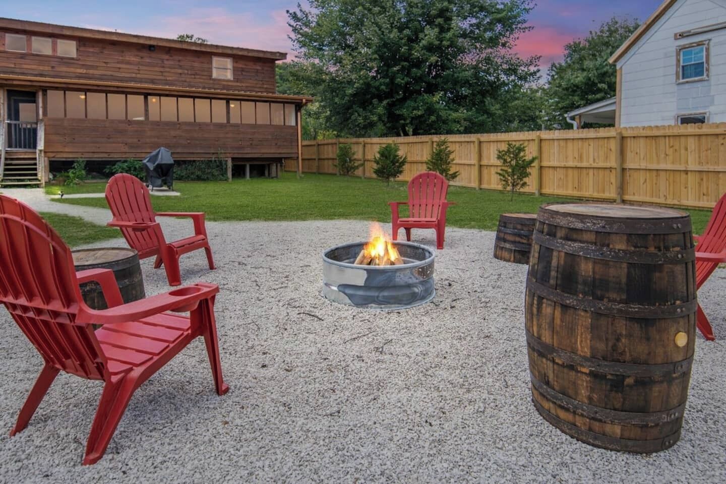 Patio trasero con un hoyo de fuego, sillas rojas y un barril de madera.