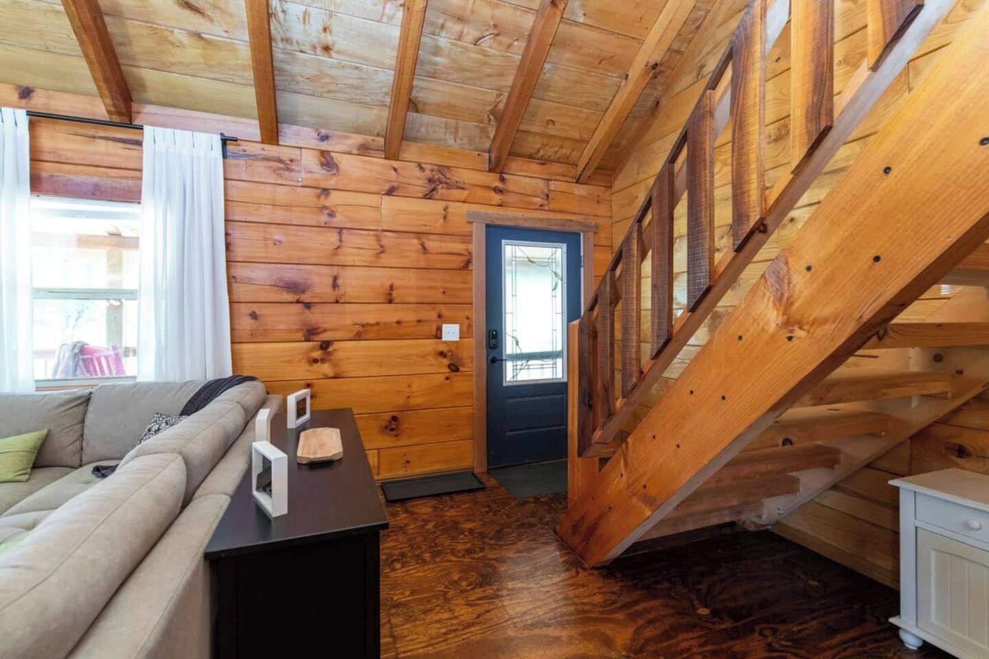 A log cabin interior with a wooden staircase, a sofa, and a small table.