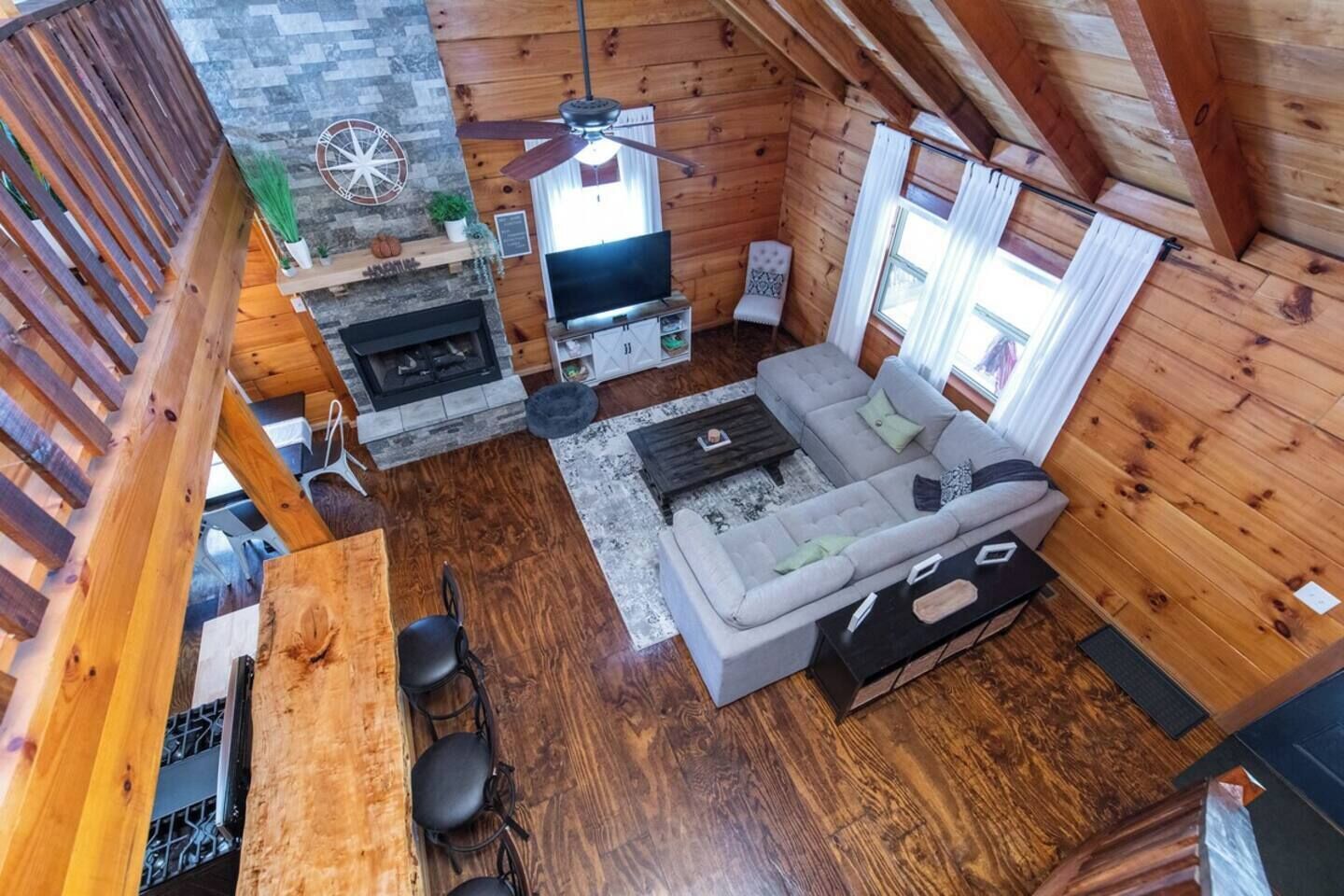 L’intérieur chaleureux d’un chalet avec une cheminée en pierre, un canapé gris et un coin repas comprenant une table et des chaises.