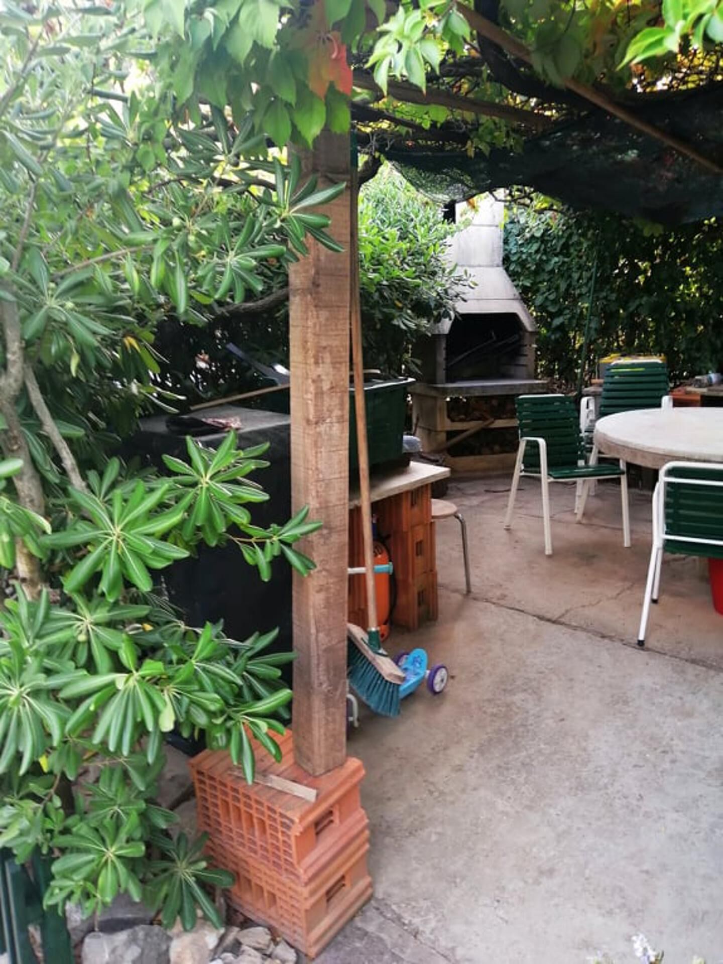An outdoor patio area with a round table and chairs, a barbecue grill, and a wooden pergola with climbing plants.