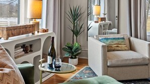 A modern living room with a green sofa, a round table with a bottle and glass, a mirror, and a lamp.