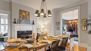 A dining area with a wooden table set for four, a fireplace, and a modern chandelier.