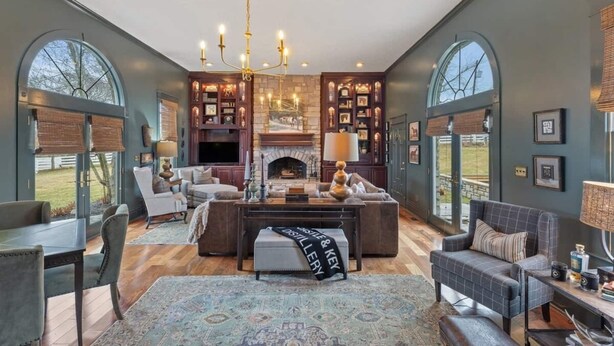 A spacious living room with a fireplace, large windows, and a chandelier.