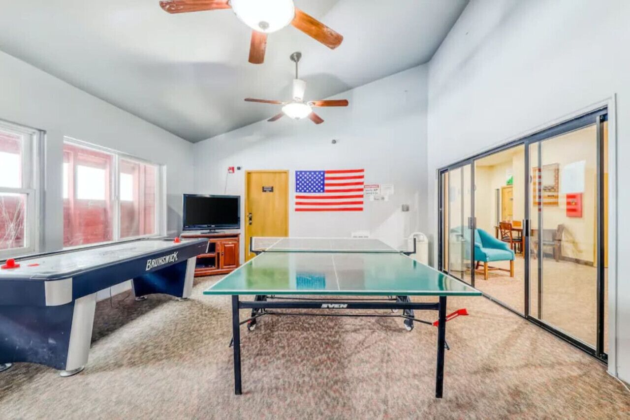Une pièce équipée d’une table de ping-pong, d’un billard, d’un ventilateur de plafond, d’une télévision et d’un drapeau américain.