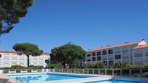 Une piscine entourée d’une clôture blanche, elle-même bordée de bâtiments aux toits rouges et aux nombreuses fenêtres.