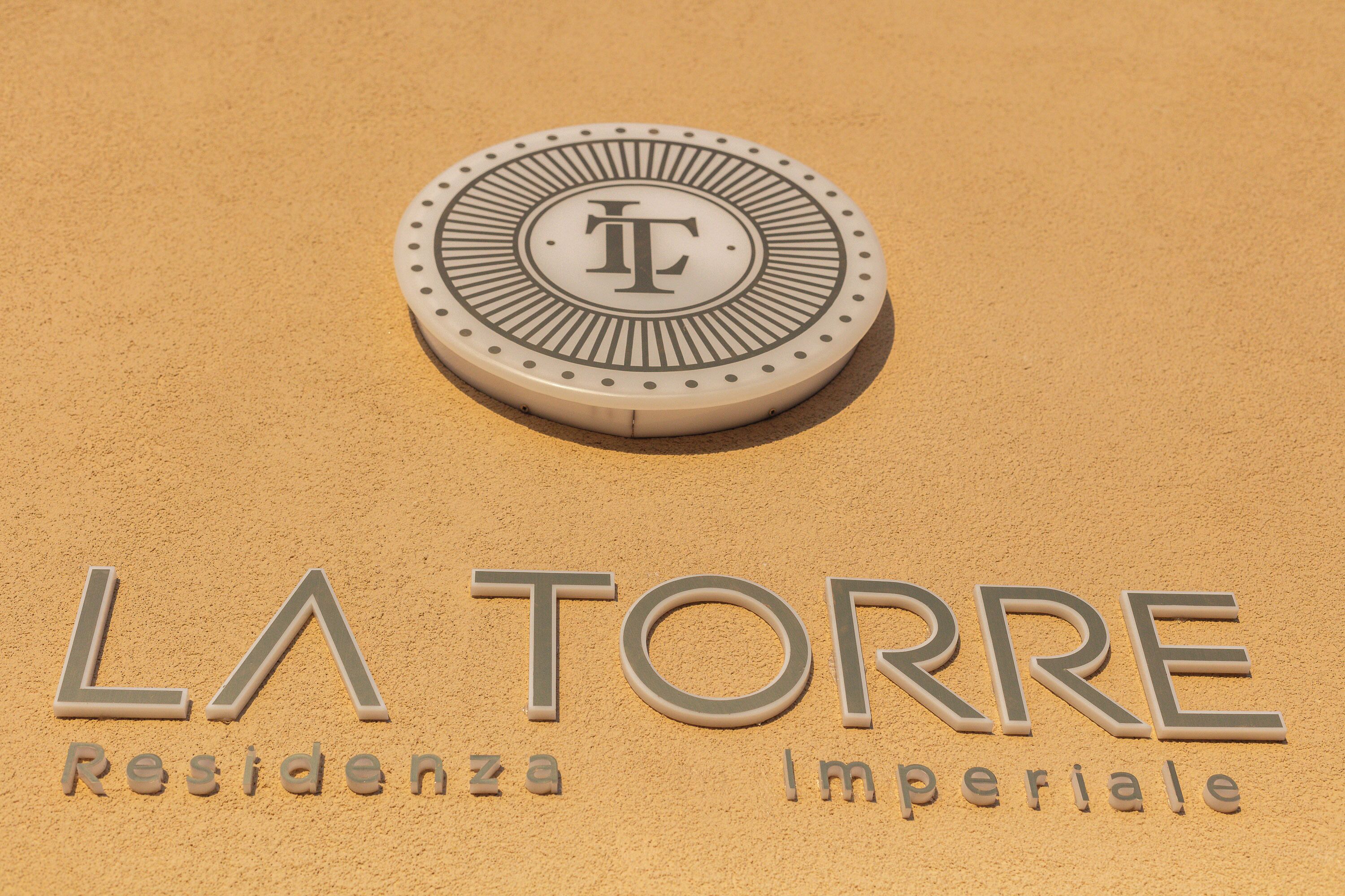 Ein Schild mit der Aufschrift 'LA TORRE Residencia Imperial' und einem runden Emblem mit dem Buchstaben 'T'.