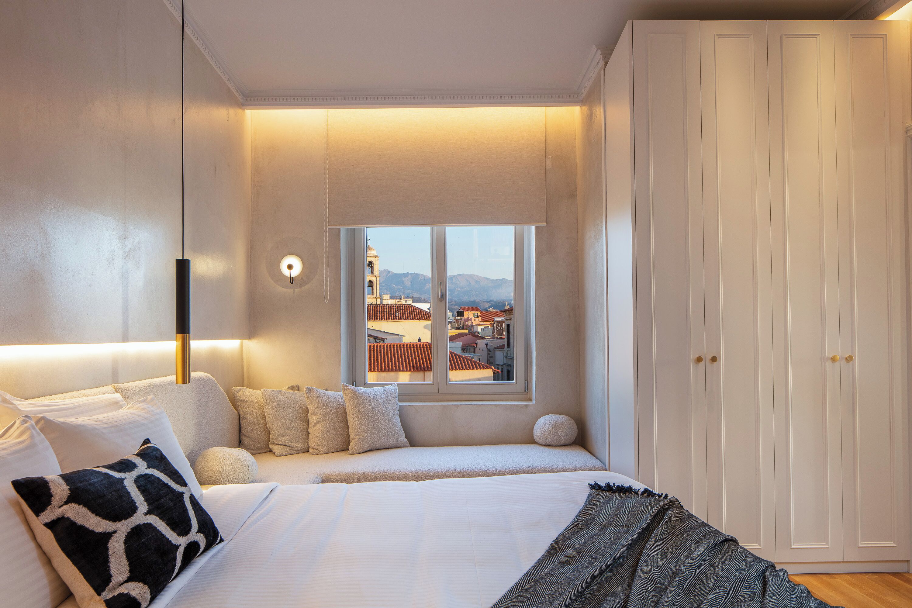A bedroom with a bed, bedside table, lamp, window, and wardrobe.