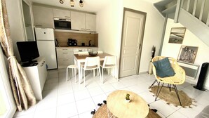 Un espacio habitable compacto con kitchenette, comedor y una pequeña zona de estar con una mesa redonda y sillas.