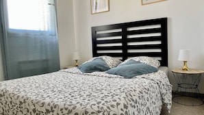 Una cama bien hecha con ropa de cama estampada, un cabecero negro, dos lámparas de noche y cuadros en la pared.