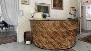 A reception area with a marble counter, framed pictures on the wall, a potted plant, and a dining area in the background. - Viale Lazzaro Papi (Rimini)